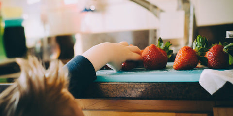 The child deftly lifting the strawberry from the table!